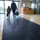 Oxford blue fine-ribbed open-grid matting laid full width across a leisure centre entrance lobby, parent and child walking in with swimming bags