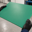 Green PE500 sheet held by gloved hands, smooth matt surface in a workshop