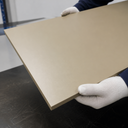 Tan-coloured PEEK sheet held by gloved hands on a dark workbench