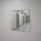 Silver polycarbonate mirror screw-fixed to a plain wall, reflecting a lit corridor with pale timber doors and strip lights