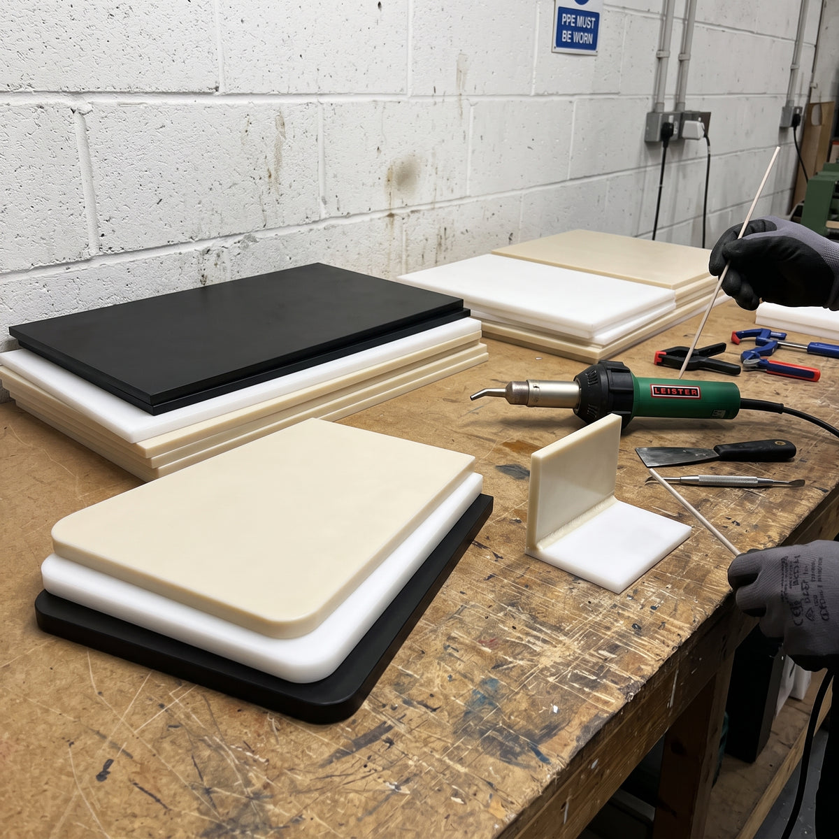 Black, white and beige polypropylene copolymer sheets stacked on a fabrication bench with a hot-air welder and a welded corner sample