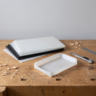Thin milky-white and black polypropylene sheets on a workbench with a shallow tray folded from one and a scoring knife