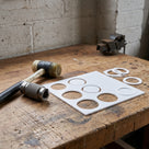 Thin white PTFE sheet on a workbench with ring gaskets punched from it, wad punch and mallet beside, bench vice behind