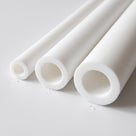 Three thick-walled white PTFE tubes of differing bores lying on white, open ends angled towards the camera
