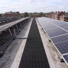 Black open-lattice PVC walkway matting laid as a maintenance path between rows of solar panels on a flat commercial roof