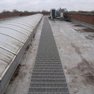 Light grey open-lattice matting in a straight run beside a long curved rooflight towards rooftop plant