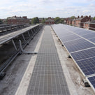 Light grey open-lattice PVC walkway matting laid as a maintenance path between rows of solar panels on a flat commercial roof