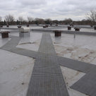 Light grey open-lattice matting running as a long path across a wide flat roof past rows of roof vents