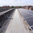 White open-lattice PVC walkway matting laid as a maintenance path between rows of solar panels on a flat commercial roof