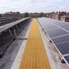 Yellow open-lattice PVC walkway matting laid as a maintenance path between rows of solar panels on a flat commercial roof