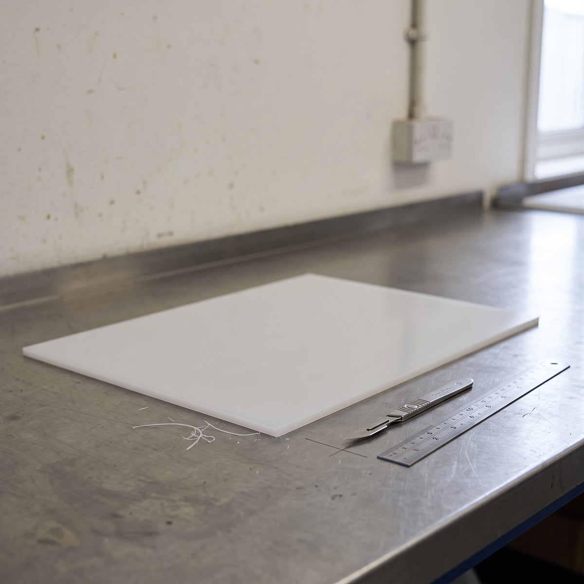 Thin translucent white PVDF sheet lying on a stainless bench with a scalpel and steel rule beside it