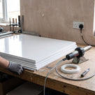 Glossy white PVDF sheets stacked on a fabrication bench with a hot-air welder, welding rod coil and knife beside them