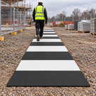 Black and white recycled-plastic pedestrian walkway mats installed on a construction site; illustrative arrangement