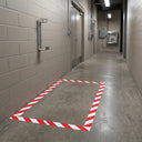 Red and white diagonal striped floor marking tape outlining a keep-clear box beneath a fire extinguisher bracket