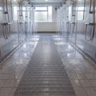 Dark grey ribbed barefoot matting running between two rows of showers in a communal shower block, water draining through the ribs