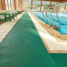 Green ribbed barefoot matting laid the length of a tiled indoor swimming pool surround beside a chrome pool ladder