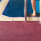 Close view of mulberry red ribbed barefoot matting at a pool edge, a swimmer stepping out of the water onto it beside the ladder rail