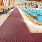 Mulberry red ribbed barefoot matting laid the length of a tiled indoor swimming pool surround beside a chrome pool ladder