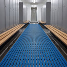Ocean blue ribbed barefoot matting runner down a changing room aisle between lockers and timber benches, wet footprints on the tiles