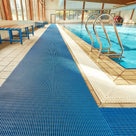 Ocean blue ribbed barefoot matting laid the length of a tiled indoor swimming pool surround beside a chrome pool ladder