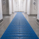 Ocean blue ribbed barefoot matting running between two rows of showers in a communal shower block, water draining through the ribs