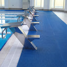 Ocean blue ribbed barefoot matting covering the deck behind a row of starting blocks at an indoor competition pool