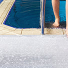 Close view of white ribbed barefoot matting at a pool edge, a swimmer stepping out of the water onto it beside the ladder rail