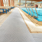 White ribbed barefoot matting laid the length of a tiled indoor swimming pool surround beside a chrome pool ladder