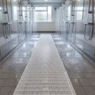 White ribbed barefoot matting running between two rows of showers in a communal shower block, water draining through the ribs