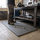 Dark grey ribbed PVC matting in front of a workshop bench with vice, dropped spanner lying on the ribbed surface