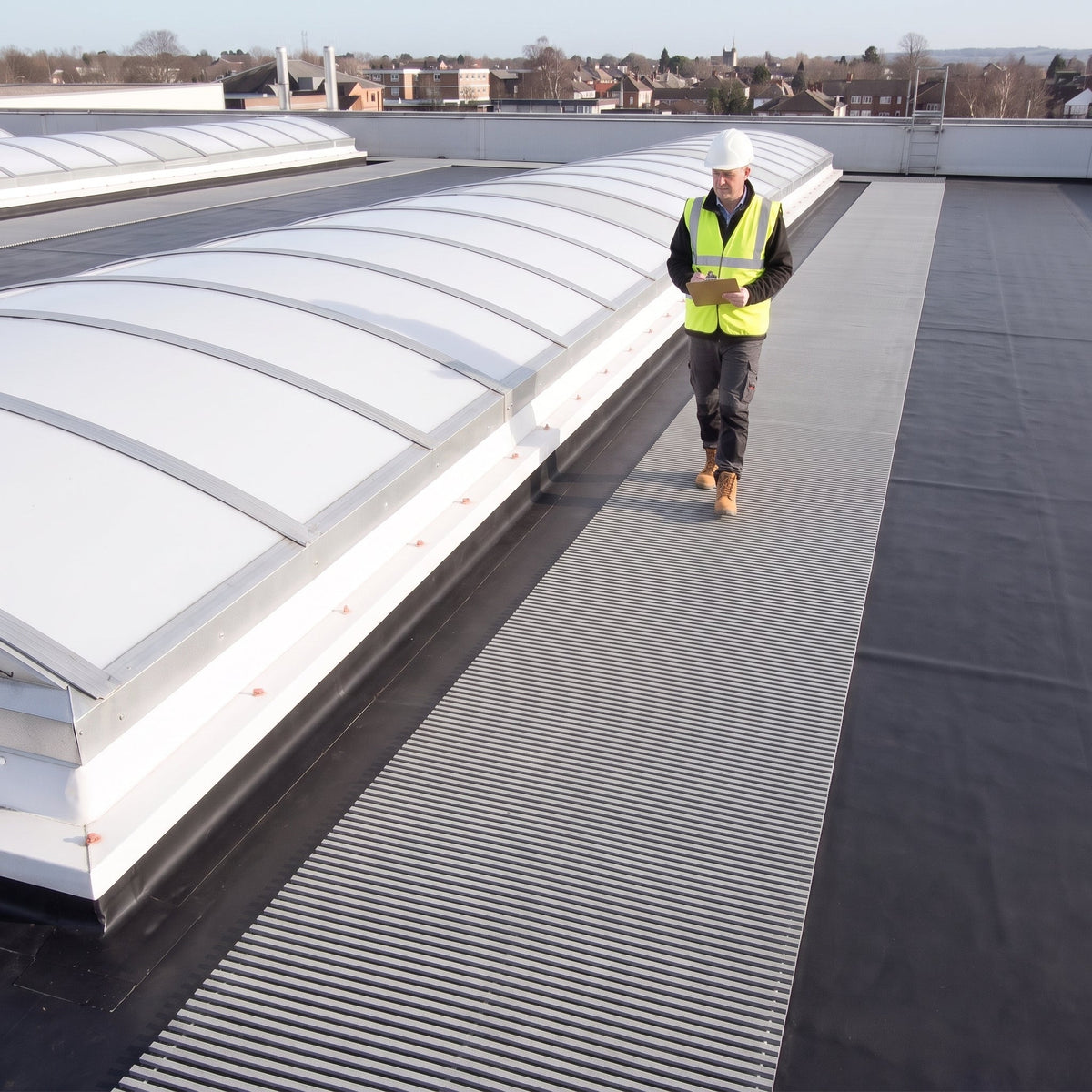 Light grey ribbed walkway matting beside barrel-vault rooflights on a dark roof, inspector carrying a clipboard