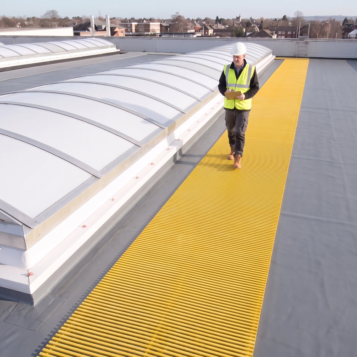 Yellow open-lattice matting beside barrel-vault rooflights on a grey membrane roof, inspector with a clipboard