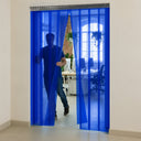 Person stepping through a blue transparent strip curtain into an open-plan office, desks beyond