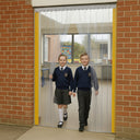 Children in school uniform walking through clear PVC strip curtains on child-safe QuickMount rail in school corridor