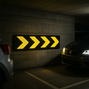 Reflective chevron wall guard mounted in UK underground car park - black rubber with yellow retroreflective arrows directing traffic