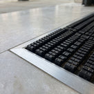 Close view of the black scraper bars topped with square grip blocks, set flush in a brushed aluminium mat-well frame with grit trapped in the channels