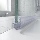 Clear seal along the bottom edge of a wet glass shower panel, bubble resting on a white tray