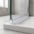 Clear seal on the bottom edge of a wet glass shower panel, bulb pressed onto a white tray