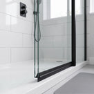 Black seal along the base of a glass shower door on a white tray, white tiles and grey mat
