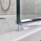 Chrome-strip seal under a wet glass screen edge on a white shower tray, marble tiles and shower hose behind