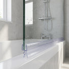Clear seal running along the bottom of a glass bath screen above a white bath, water-speckled glass