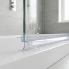 Clear seal running along the base of a glass bath screen on a white bath, chrome taps and grey tiles