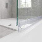Clear seal along a wet glass screen edge on a white shower tray, water running down, chrome valve behind
