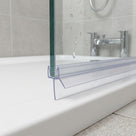 Clear seal on a glass bath screen edge, long blade lying on the white bath rim, chrome taps behind