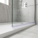 Clear seal along the base of a water-speckled glass enclosure on a white tray, grey tiles behind