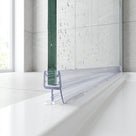 Clear seal along the bottom edge of a wet glass shower panel, blade flat on a white bath rim