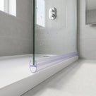Clear seal along the bottom edge of a glass shower panel meeting a white tray, wet glass behind