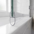 Clear seal along the bottom edge of a curved glass bath screen, teardrop bubble resting on the white bath rim, metro tiles