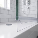 Clear seal along a glass door bottom edge on a white bath, white metro tiles and shower behind