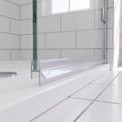 Clear seal on the bottom edge of a glass shower door, rigid fin on a white tray, metro tiles behind